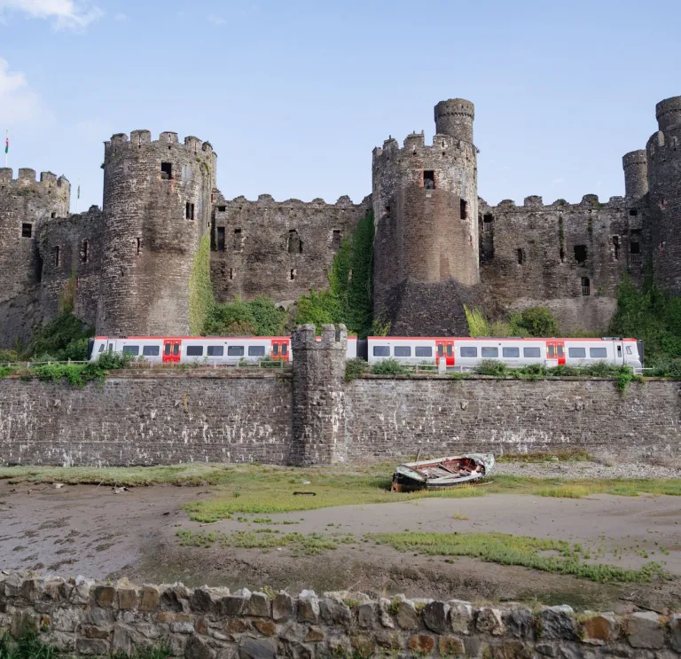 A train passing a castle next to the shoreline.