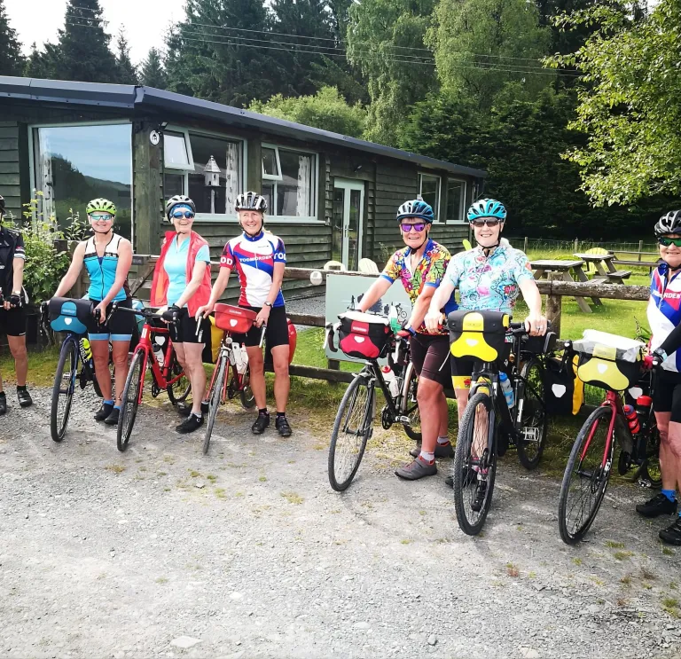 A group of cyclists outside a wooden lodge surrounded by trees. 