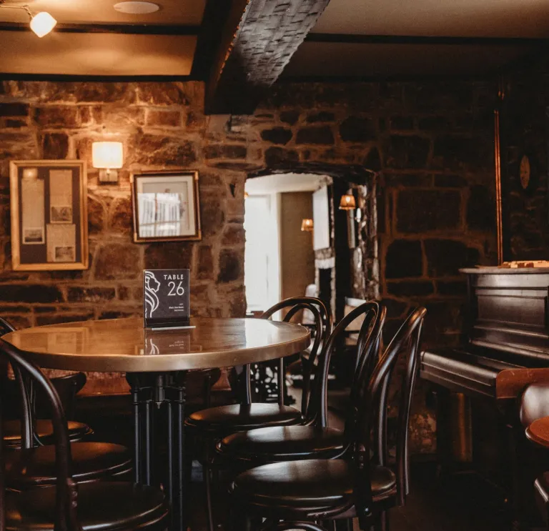 Tables, chairs and a piano in a stone walled lounge area of a hotel.