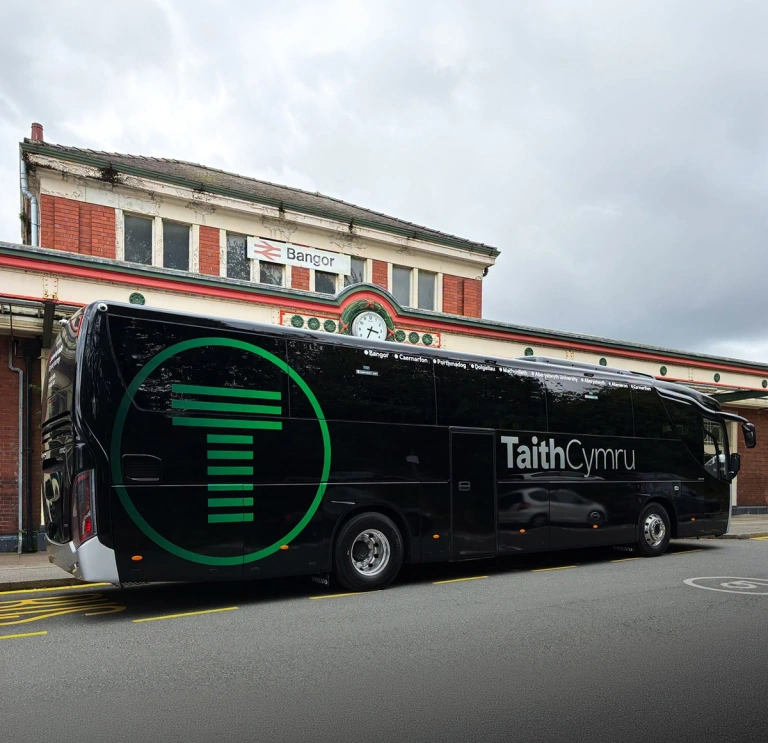 A coach parked up outside a train station.