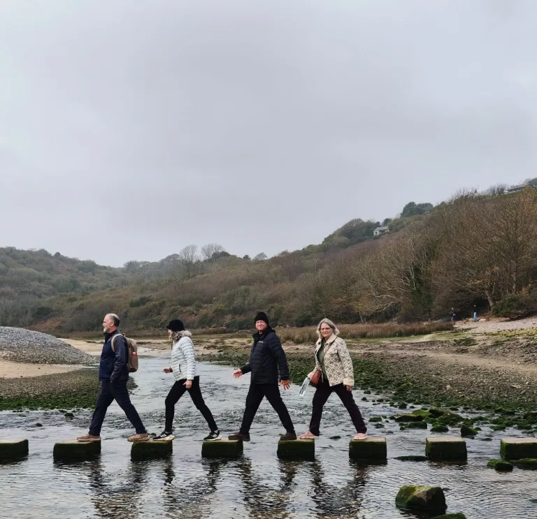 Group of people walking on stepping stones over a river.