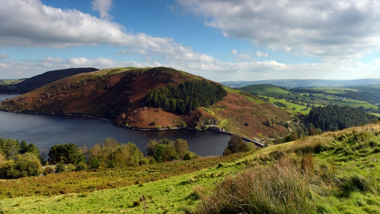 Landscape image of a reservoir, surrounded by a mountain and trees.