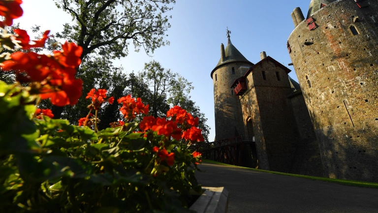 Flowers in bloom next to the path of a castle entrance.