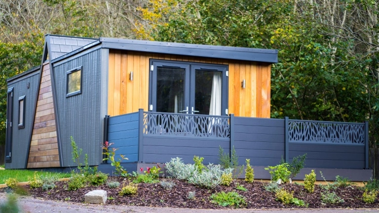A blue wooden four berth lodge in a forest park.