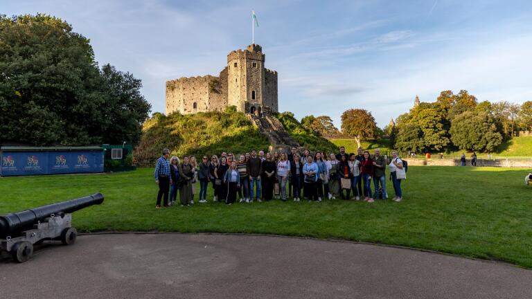 Group of people standing at the foot of a castle smiling at the camera.