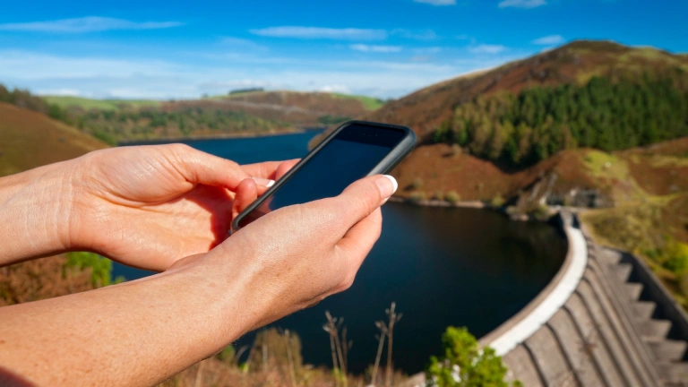 Female walker using iPhone near a reservoir.