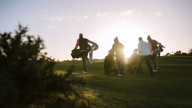 Golfers walking to the next tee on a golf course at sunrise.