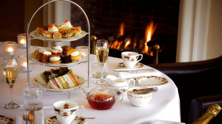 A table set up for afternoon tea with champagne next to a roaring fire.