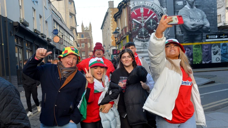 Supporters on match day wearing Welsh shirts and hats walking down the street.