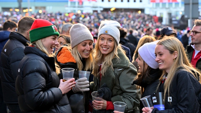 Group of ladies holding drinks and laughing, outside a sports stadium .