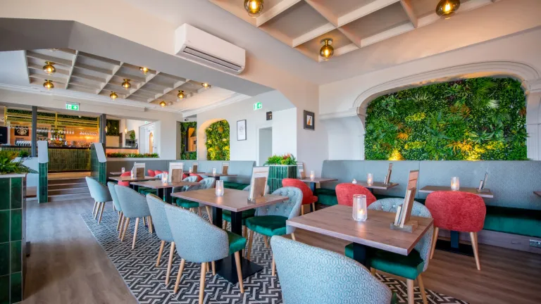 Hotel restaurant with small tables and chairs and greenery