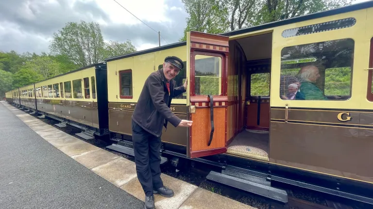 Man holding open a door of train carriage on a steam train.