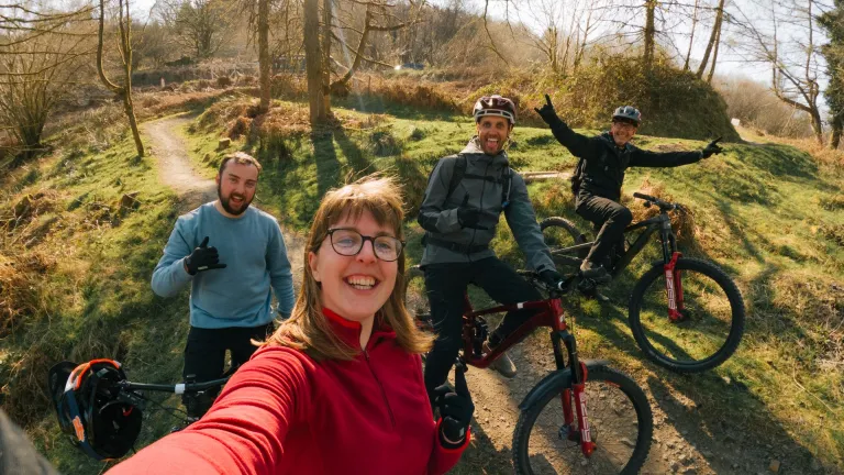 Group of people with their bikes in a bike park smiling at the camera.