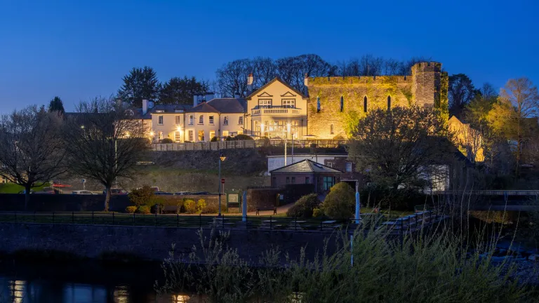External shot of a castle hotel lit up at night, with a river running beside it.