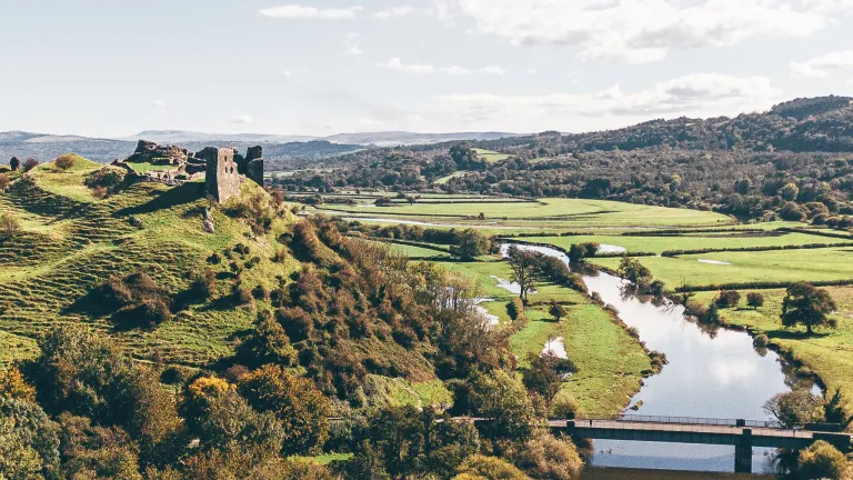 A castle on a hill with views alongside a river surrounded by countryside.