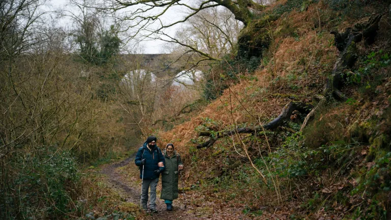 A couple walking along a forest footpath with a viaduct in the background.