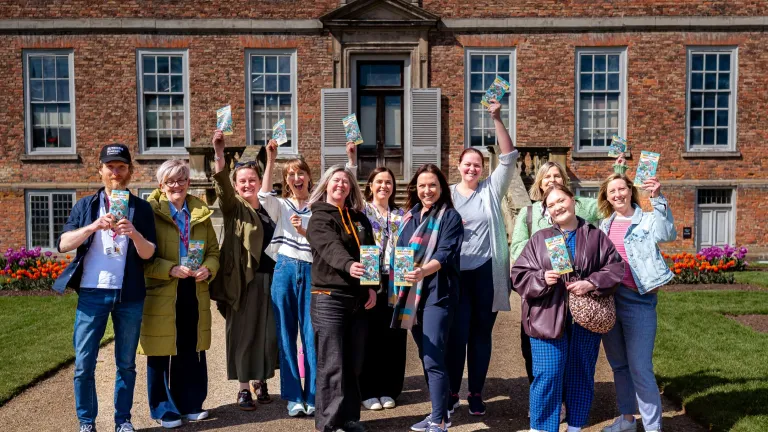 A group of people outside an grand estate holding visitor attraction leaflets.