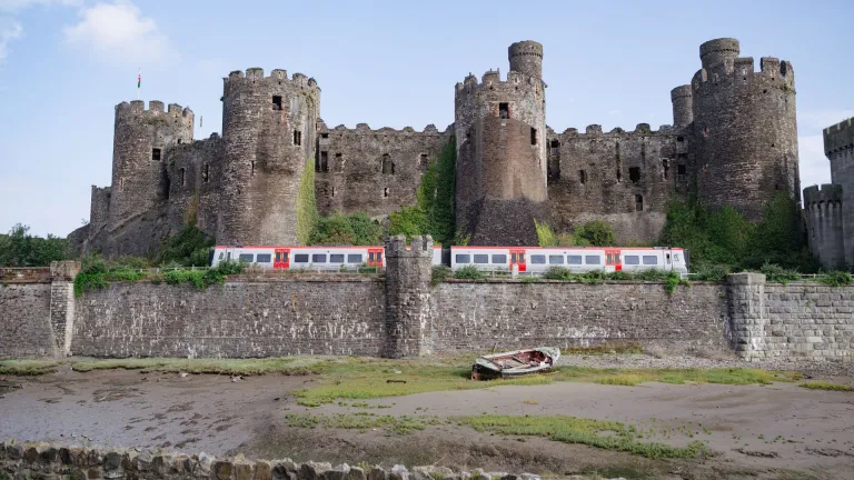 A train passing a castle next to the shoreline.