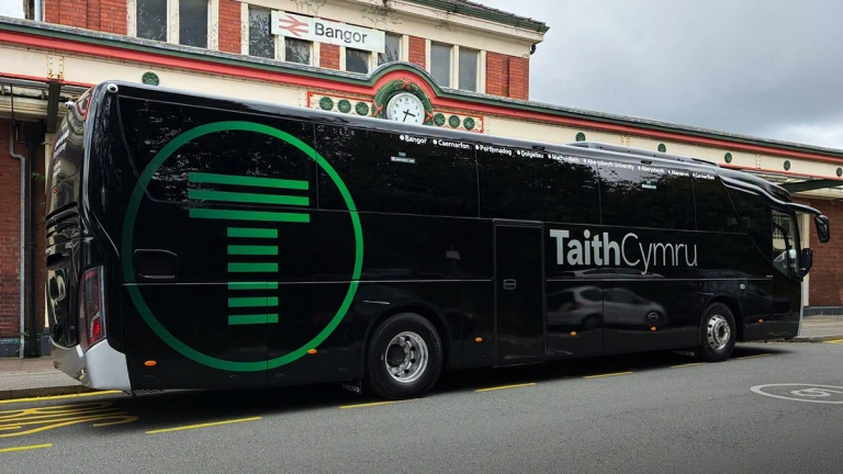 A coach parked up outside a train station.