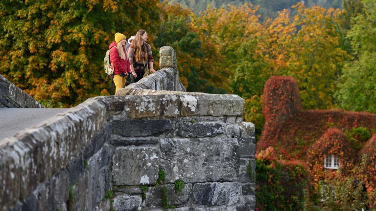 A small group of people on a bridge by Tu Hwnt I'r Bont in autumn.