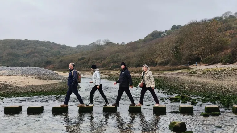 Group of people walking on stepping stones over a river.