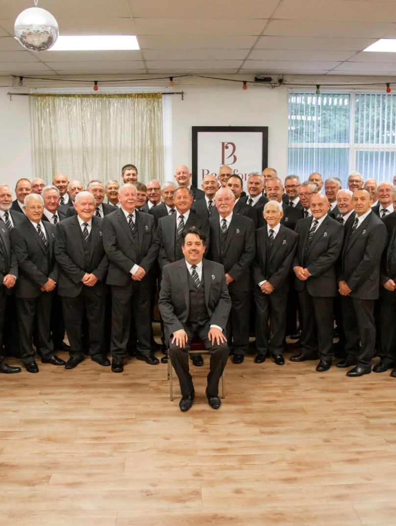 A large group of male singers in suits smiling at the camera.