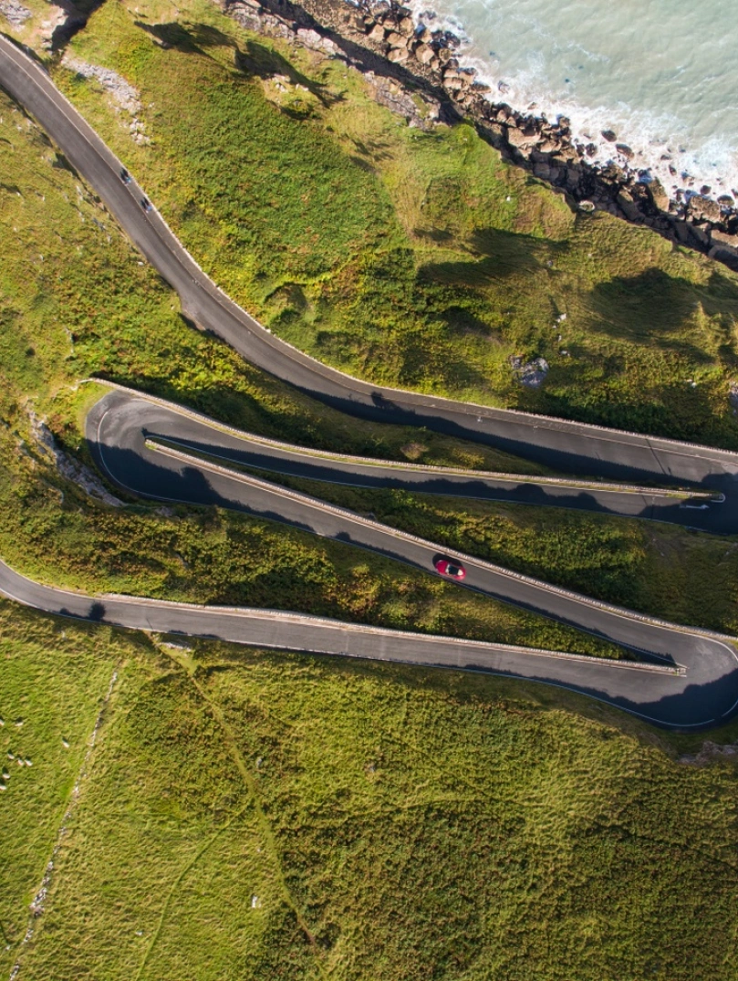 A car driving a zig zag road on a headland by the coast.
