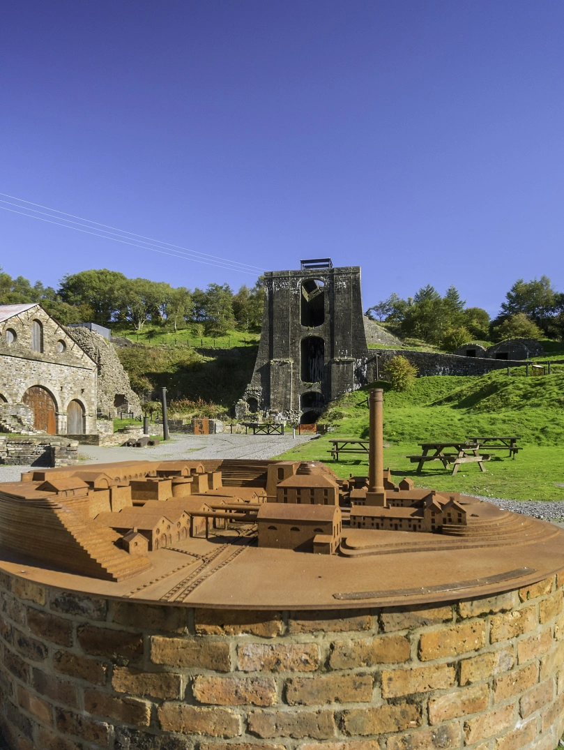 A small scale model of the ironworks at Blaenavon, with real site behind it.