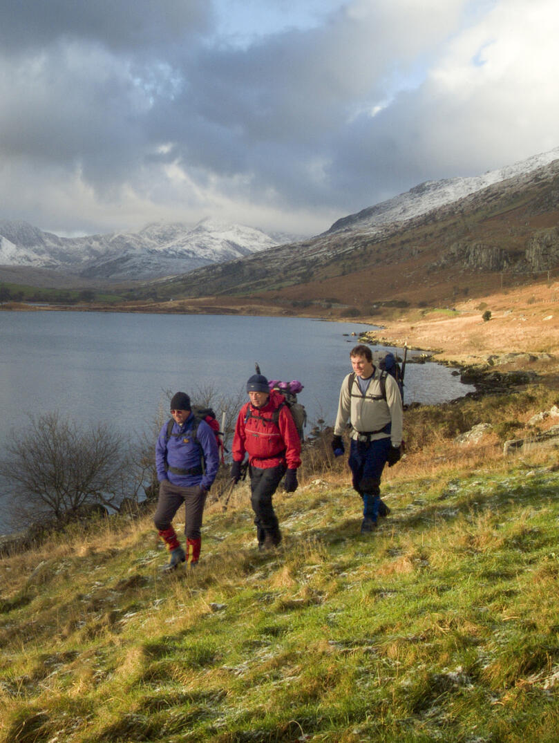 Three walkers taking a walk along the Llynnau Mymbyr lake in Snowdonia.