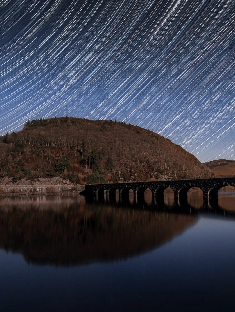 Star trails in the night sky above a reservoir.