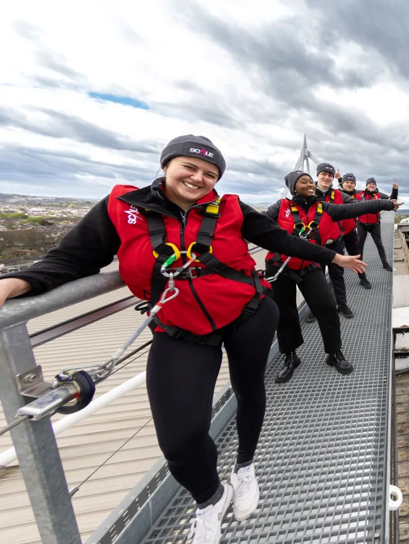 Group of people in safety gear on a roof at a sports stadium.