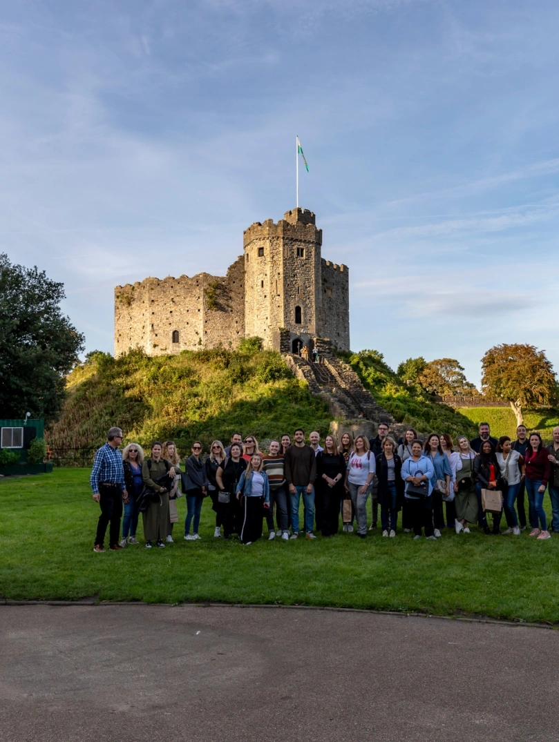 Group of people standing at the foot of a castle smiling at the camera.