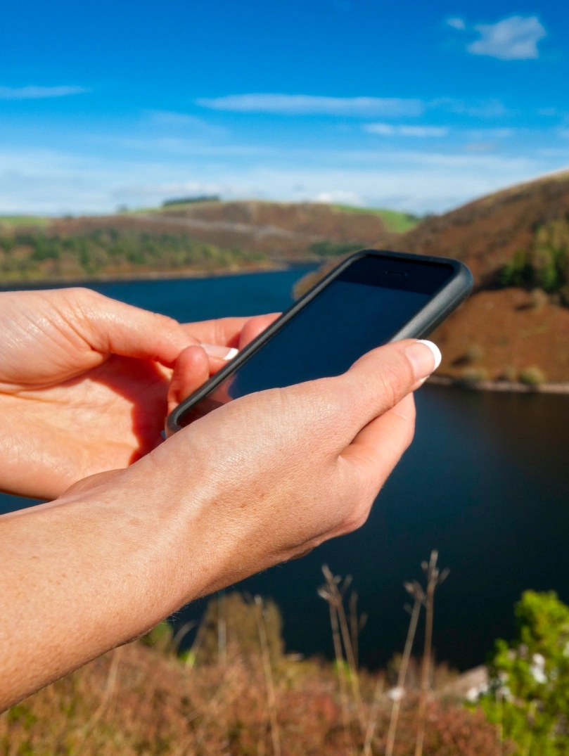 Female walker using iPhone near a reservoir.
