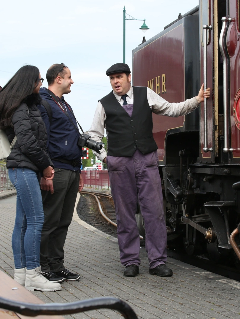 A couple talking to the driver next to a steam train.