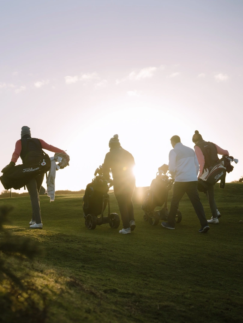 Golfers walking to the next tee on a golf course at sunrise.