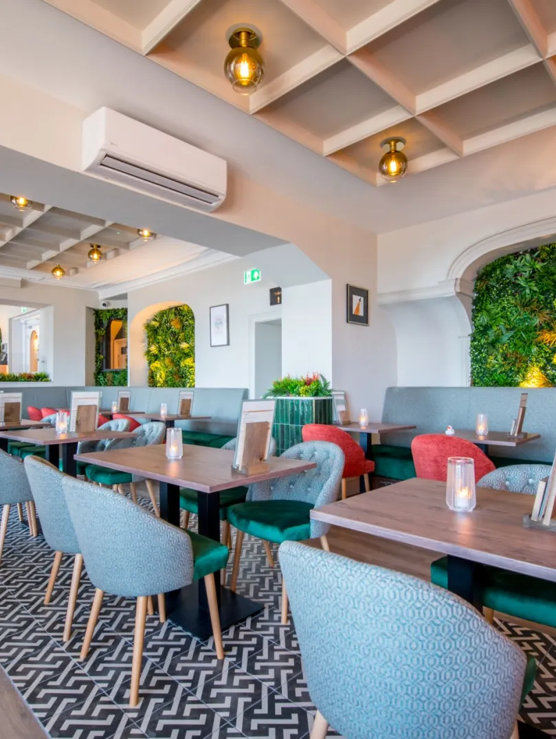 Hotel restaurant with small tables and chairs and greenery