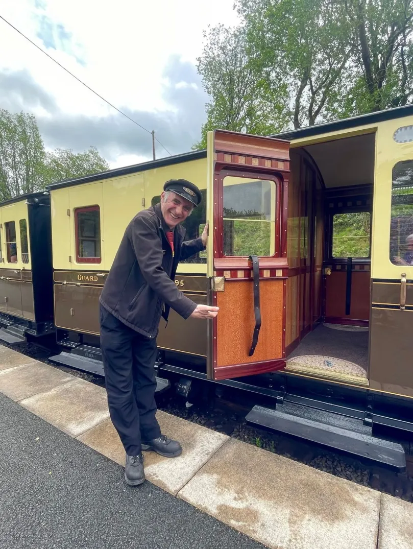 Man holding open a door of train carriage on a steam train.