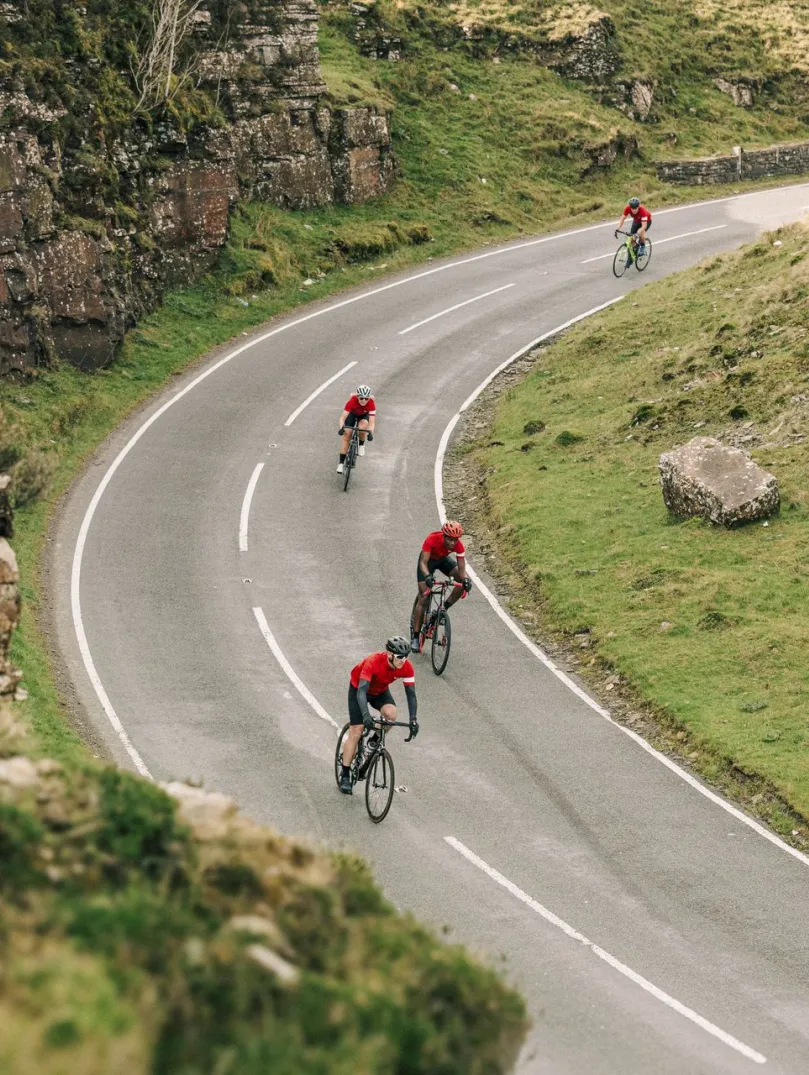 Cyclists on a road against a mountainous landscape with a Welsh dragon on the wall.