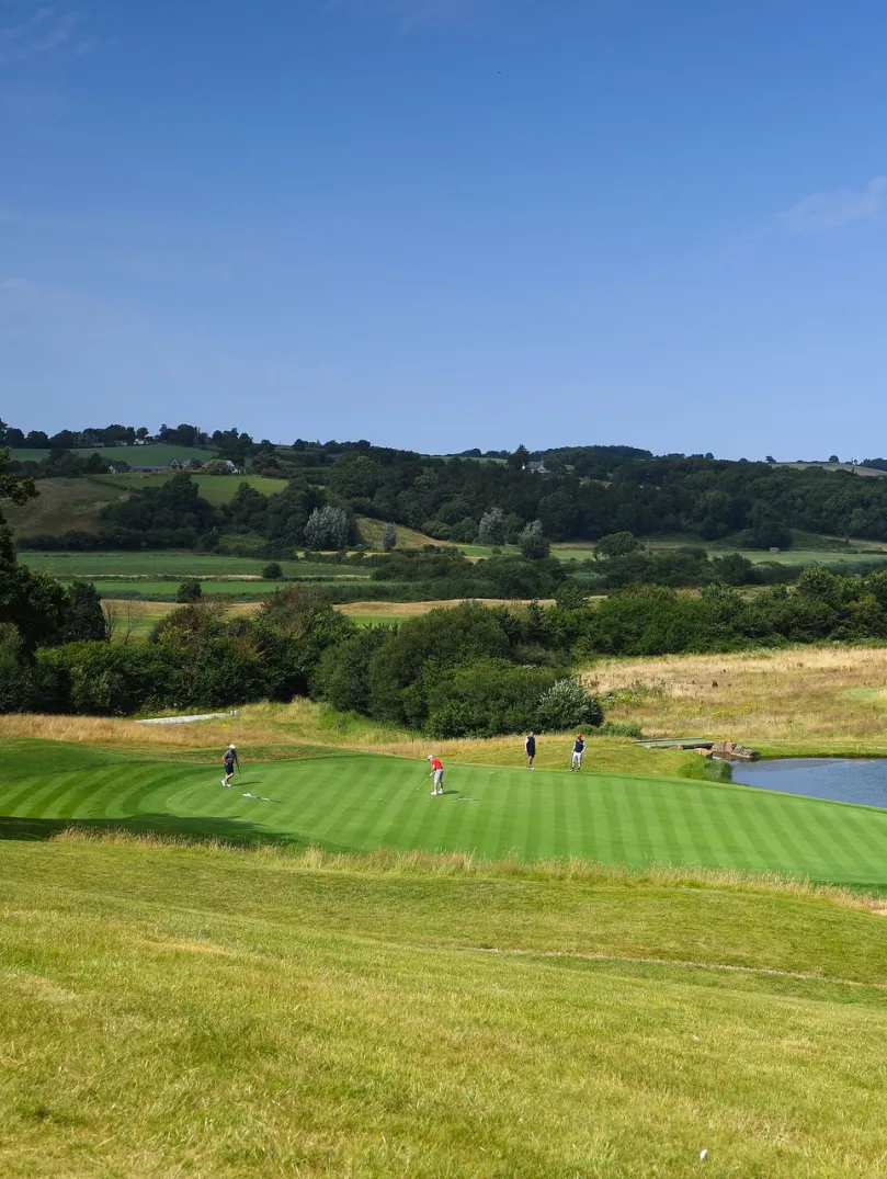 Golfers putting on the green of a golf course next to a fountain.