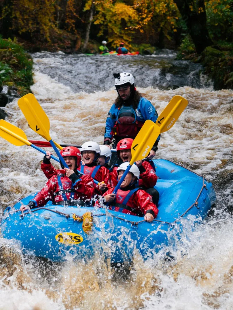 Group of people on a raft heading down rapids on a river.
