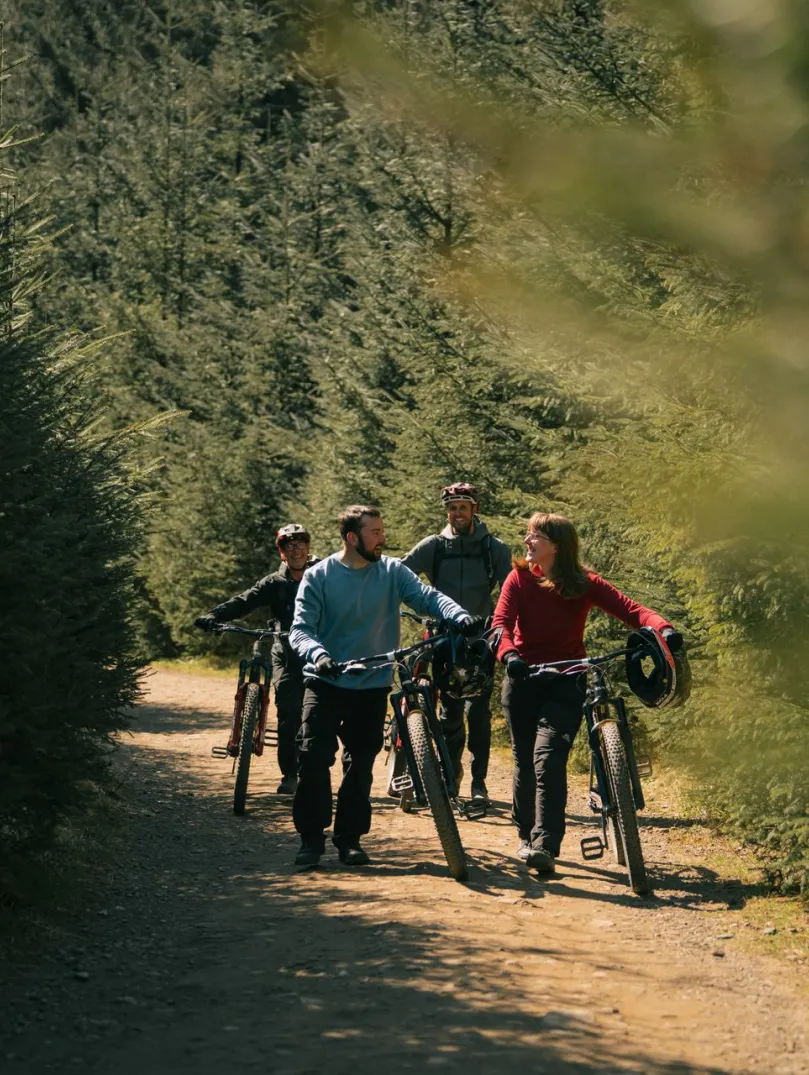 Four cyclists walking their bikes in a forest.