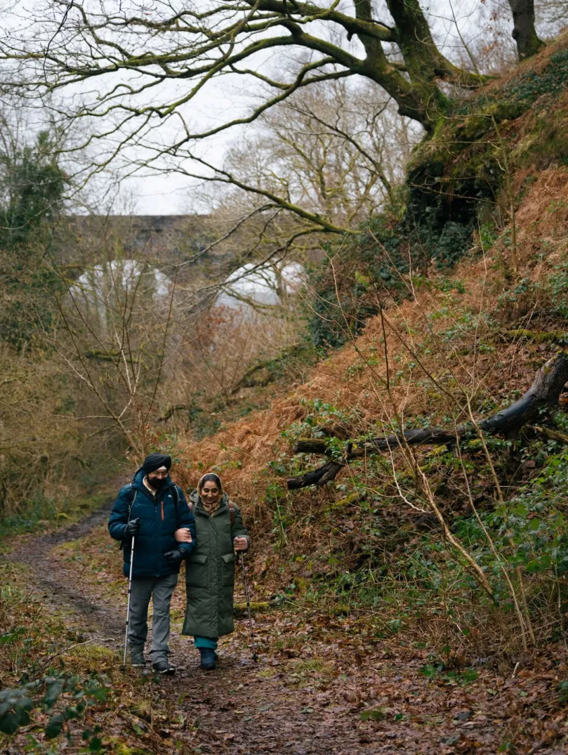 A couple walking along a forest footpath with a viaduct in the background.