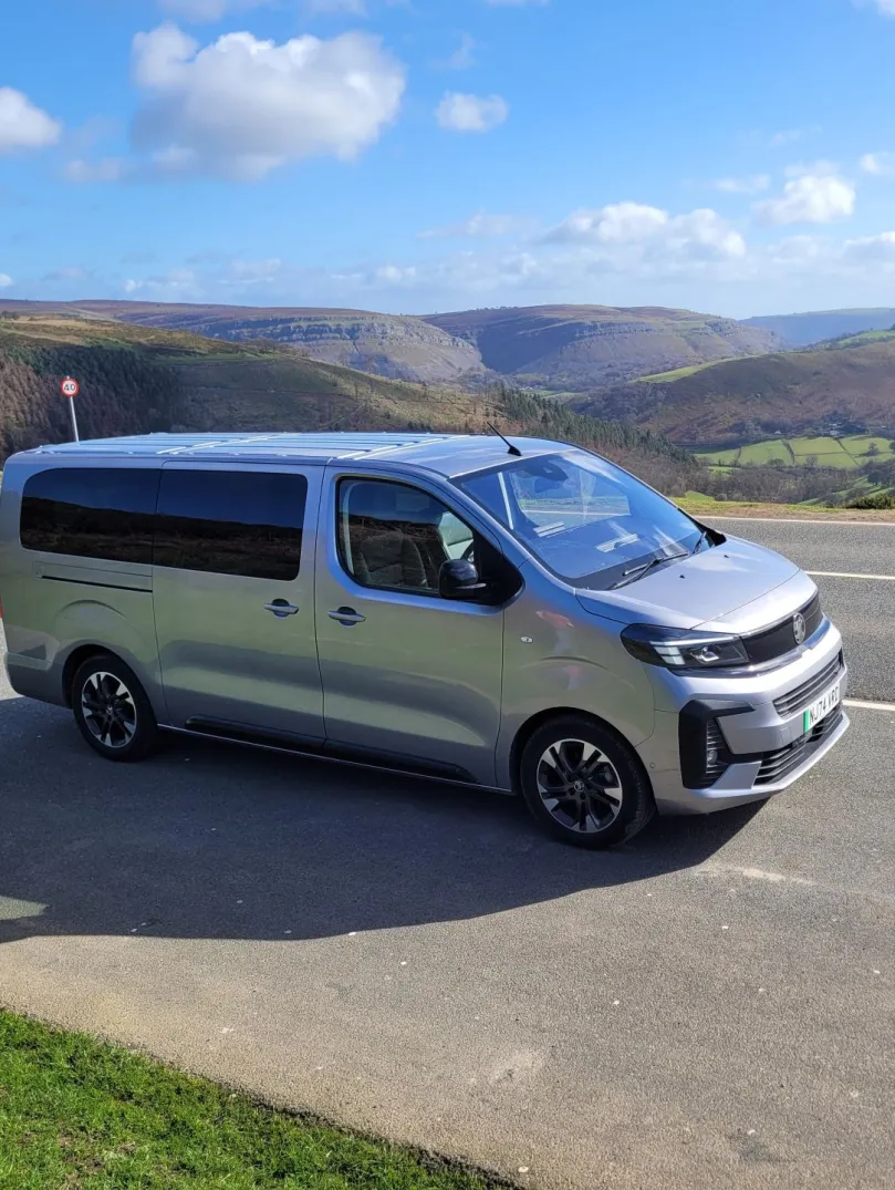 Minibus parked on an open road with a backdrop of spectacular mountains.