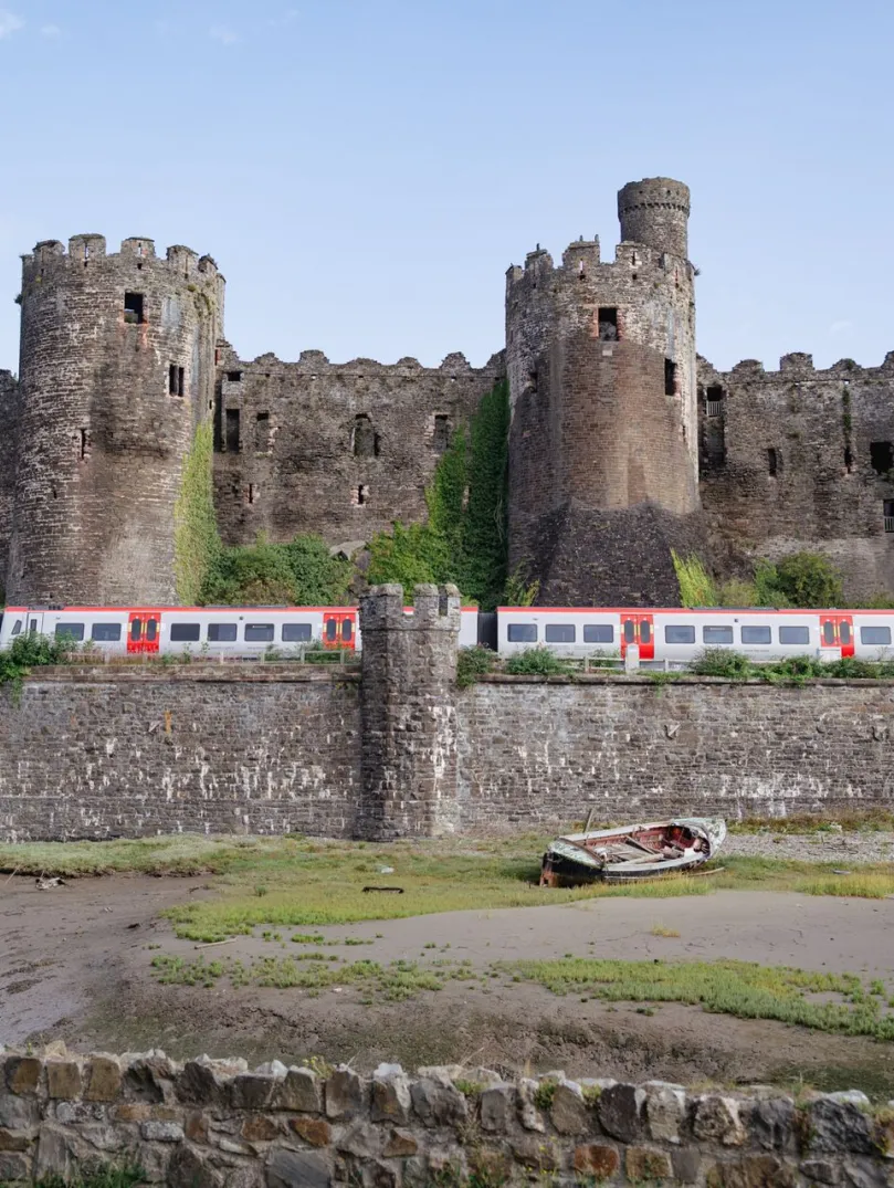 A train passing a castle next to the shoreline.