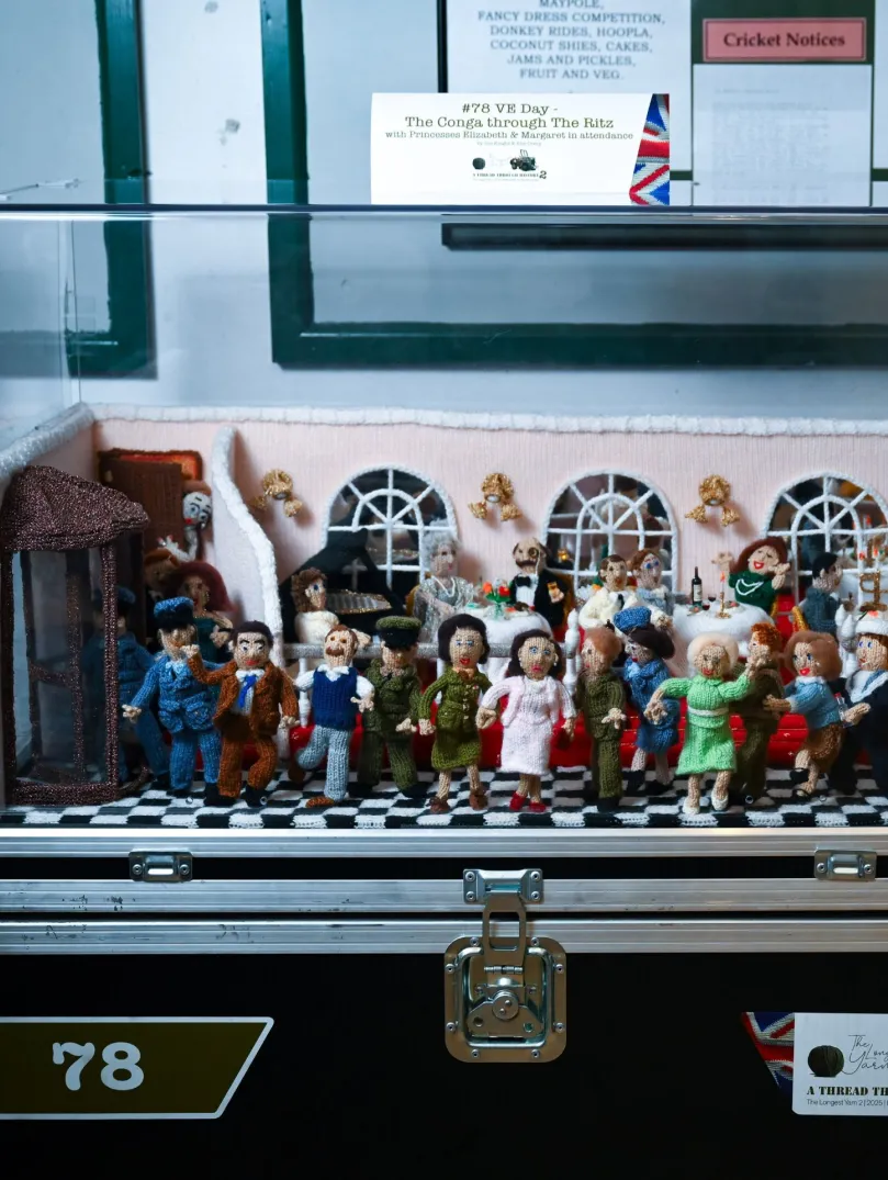 A lady sitting next to a display of knitted characters