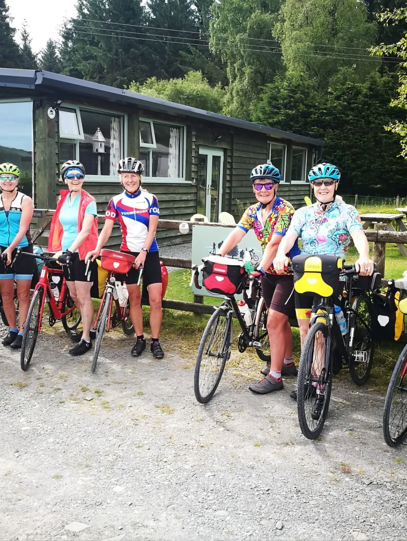A group of cyclists outside a wooden lodge surrounded by trees. 