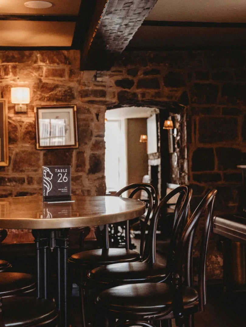 Tables, chairs and a piano in a stone walled lounge area of a hotel.