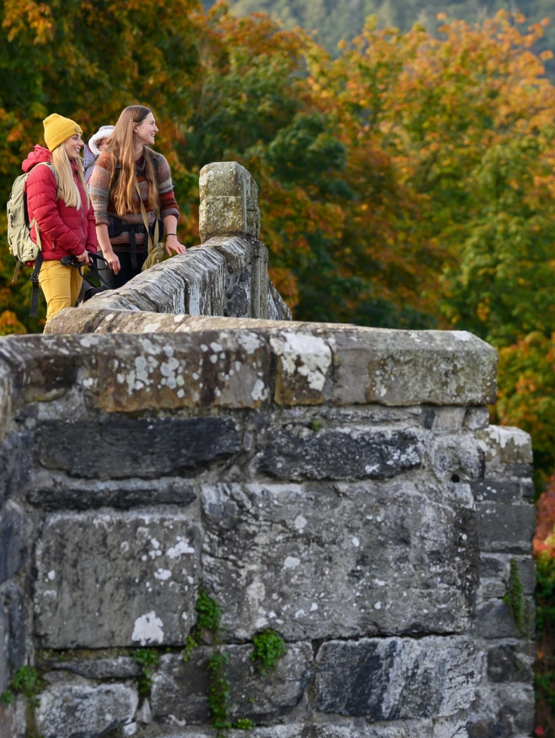 A small group of people on a bridge by Tu Hwnt I'r Bont in autumn.