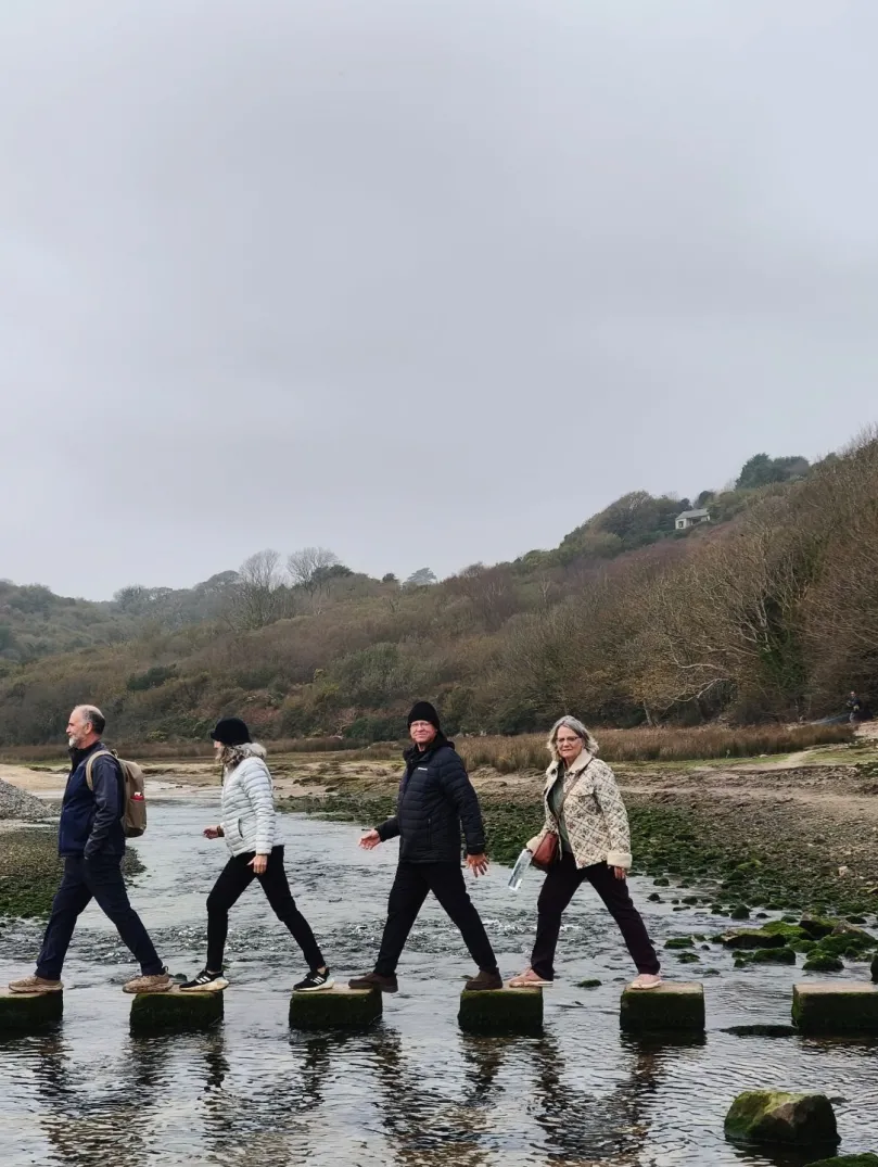 Group of people walking on stepping stones over a river.