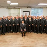 A large group of male singers in suits smiling at the camera.